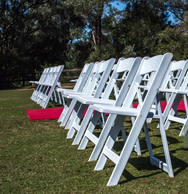 Rows of white folding chairs beside a red wedding carpet outdoors